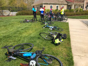 a group of bicyclists standing around their bikes on the grass