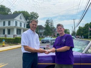 two men shaking hands in front of a purple car
