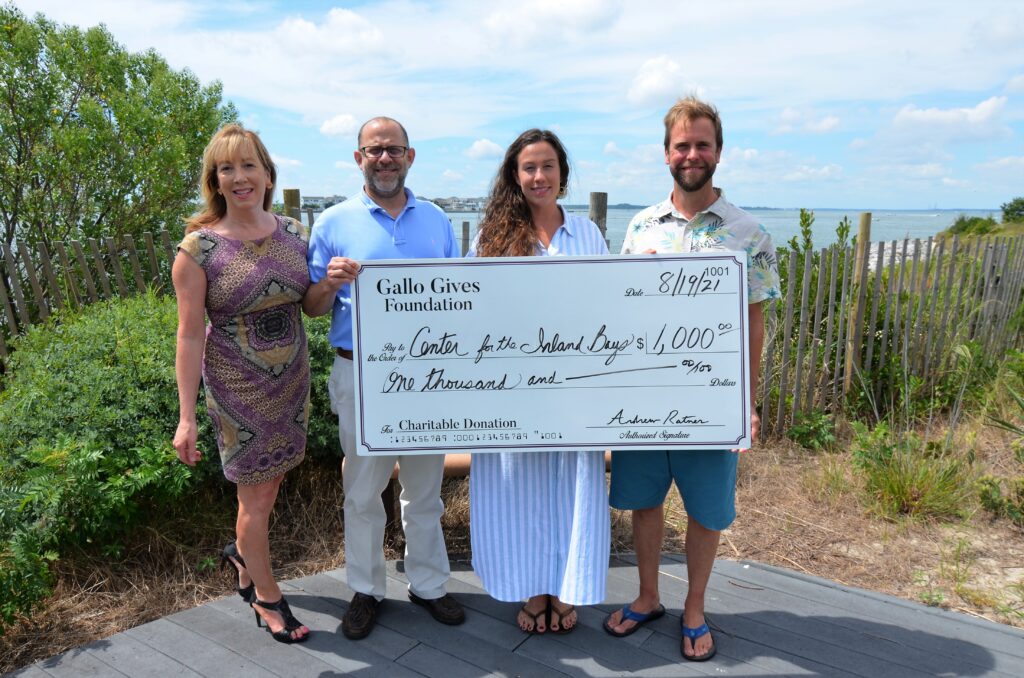 three people holding a large check in front of the ocean