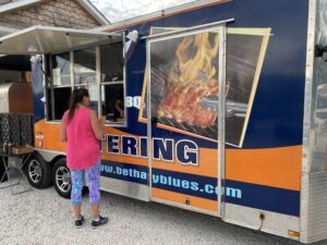 a woman standing in front of a blue and orange food truck
