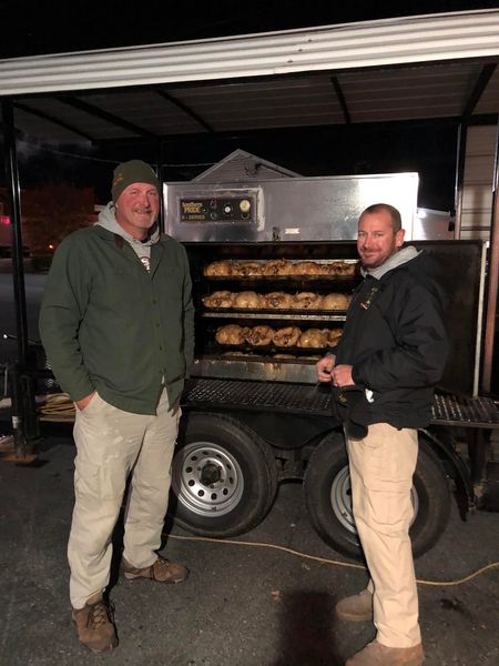 two men standing next to each other in front of a grill