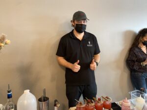 a man wearing a face mask standing in front of a table with drinks
