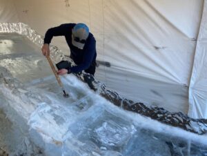a man in a blue jacket is working on an ice sculpture