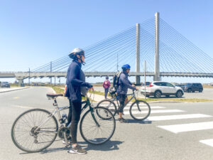 two people on bicycles crossing a street in front of a bridge