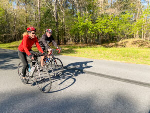 two people riding bikes down a road in the woods