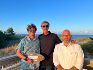 three men standing on a deck near the ocean
