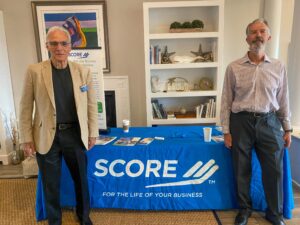 two men standing next to a table with a score sign on it