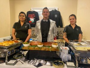 three people standing behind a buffet table with food