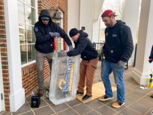three men unloading a bag of ice from a cart