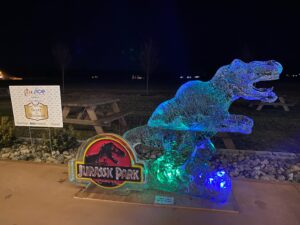 a lit up dinosaur park sign in the middle of a field