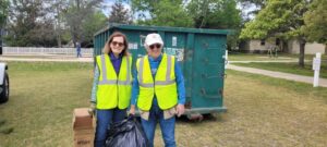 two people in safety vests standing next to a dumpster