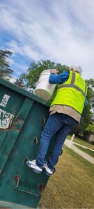 a man in a safety vest is dumping a can into a dumpster
