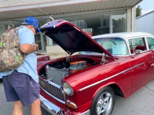 a man with a backpack looking under the hood of an old car