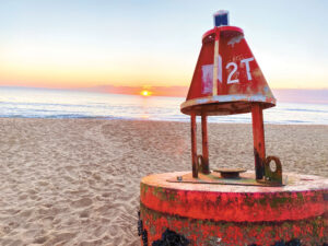 a red and white fire hydrant sitting on top of a sandy beach