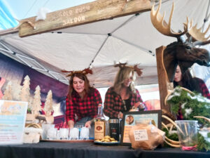 two women standing behind a table with bottles and deer heads on it