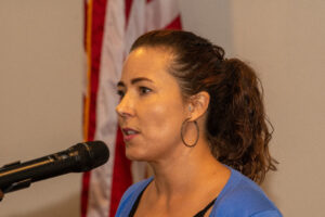 a woman speaking into a microphone in front of an american flag