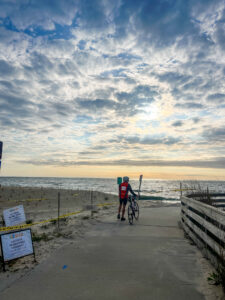 a person on a bike walking down a path to the beach